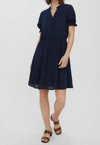 Mörkblå klänning med korta puffärmar, knappad fram, elastisk midja och en flödande kjol. Bärs med bruna remsandaler.