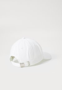 Witte katoenen pet met een gebogen klep, verstelbare metalen gesp aan de achterkant en gestikte ventilatiegaten op een glad, onopvallend oppervlak.