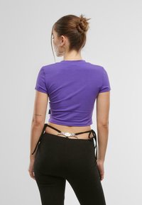 Violeta īsā T-krekls, izgatavots no gludas auduma, ar īsām piedurknēm, apvienots ar melniem pieguļošiem biksēm, kurām ir dekoratīva saite un metāla detaļas.