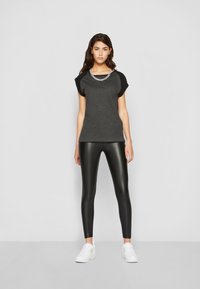 Behagelig grå T-skjorte med svarte korte ermer og et metallkjede, kombinert med blanke sorte leggings og hvite joggesko.