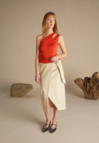Top rojo de un solo hombro con fruncidos, combinado con una falda beige con una abertura lateral y un lazo decorativo. Bailarinas negras de punta con tachuelas.