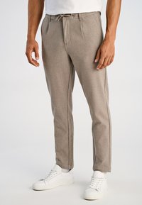 Beige op maat gemaakte broek van gestructureerde stof, met een taillekoord en zijzakken. Gecombineerd met witte sneakers.