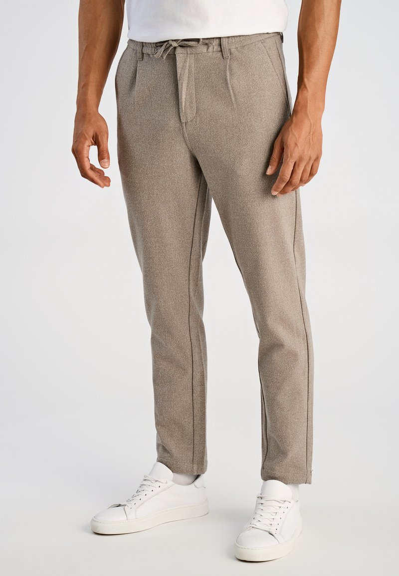 Beige op maat gemaakte broek van gestructureerde stof, met een taillekoord en zijzakken. Gecombineerd met witte sneakers.