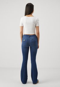 Vit kort topp och mörkblå utsvängda jeans med en subtil stretch, utrustade med bakfickor och en svart etikett på höger ficka.