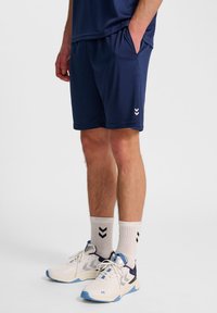 Granatowe szorty sportowe z elastycznym pasem, połączone z białymi i niebieskimi butami sportowymi oraz białymi skarpetkami z czarnymi wzorami w zygzak.