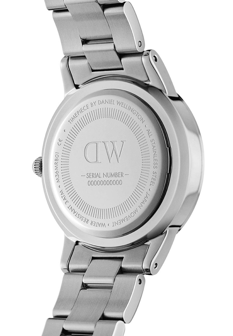 Fond de montre en acier inoxydable présentant le logo gravé "DW", le numéro de série et des détails sur l'étanchéité. Surface lisse et polie avec finition métallique.