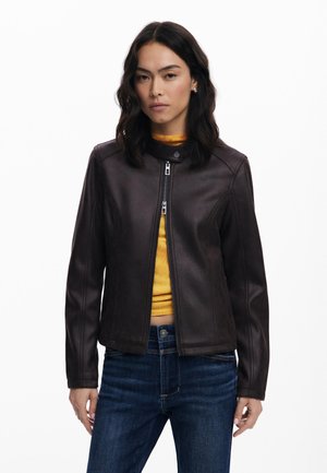 Giubbotto di pelle marrone con colletto rotondo, chiusura con zip e dettagli sulle cuciture laterali. Indossato sopra un top giallo e abbinato a jeans blu.