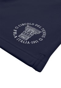 Tissu bleu marine affichant un emblème blanc avec une colonne classique et le texte "Circolo del Tennis FILA Italia 1911" l'entourant.