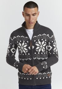 Grauer Reißverschluss-Pullover mit weißen Schneeflockenmustern, gerippten Bündchen und Saum; ausgestattet mit einem Holz-Reißverschluss-Zipper und einem kleinen Markenlabel am Saum.