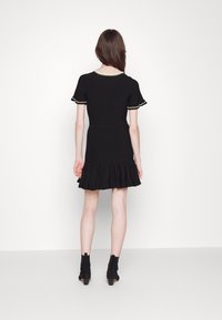 Schwarzes geripptes Kleid mit kurzen Ärmeln und gerafftem Saum. Hat einen runden Halsausschnitt mit kontrastierendem Besatz. Getragen mit schwarzen Knöchelstiefeln.
