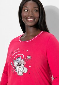 Chemise rouge à manches longues avec un graphisme d'un chat jouant avec une pelote de laine dans un panier, agrémentée de cœurs et du texte « J'adore les câlins ». Texture lisse.