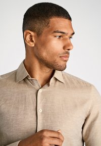 Licht beige linnen overhemd met een boord met knopen. Heeft een gestructureerde stof en een subtiele glans, zichtbare knoopsluiting en opgevouwen manchetten.