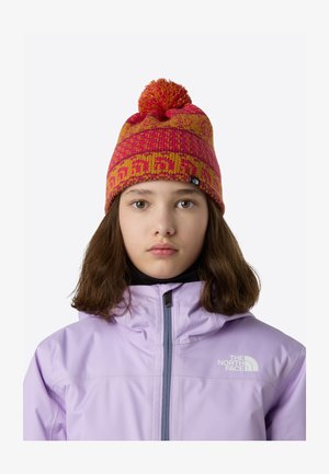 Pisano pletena kapa v roza in rumeni barvi s cofom na vrhu. Vzorec vključuje geometrične motive in črno oznako blagovne znamke na strani.