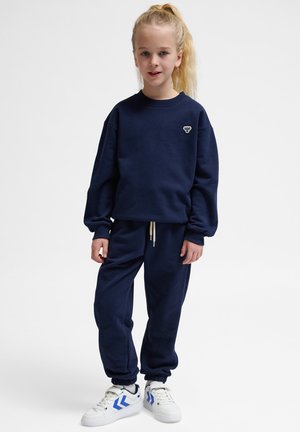 Marineblå sweatshirt og matchende joggers lavet af blødt stof; har dropped shoulders og elastiske manchetter. Skarpe sneakers med blå accenter.