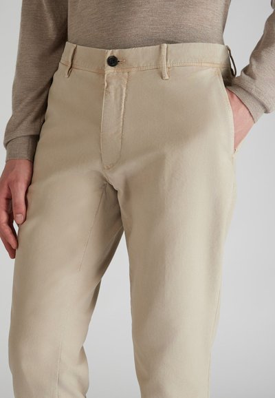 Pantalones de algodón beige con una textura suave, que cuentan con un botón frontal y bolsillos laterales. El diseño incluye sutilezas en los detalles de costura.