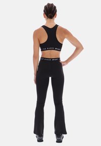 Čierna športová podprsenka a zodpovedajúce rozšírené legíny s bielym označením "TED BAKER SPORT" na páse. Hladká štruktúra, športový dizajn.