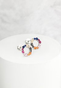 Färggranna cirkulära örhängen med olika ädelstenar, inklusive blå, svart, rosa och orange, infattade i silverfärgad metall. Cirkulär design.