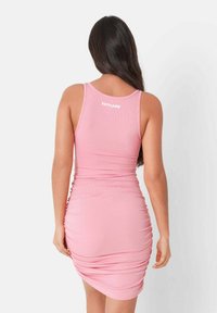 Abito bodycon rosa a coste con dettagli arricciati, caratterizzato da un scollatura a barca e logo bianco sul retro. Tessuto morbido e forma aderente.