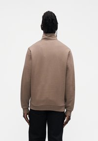 Brązowa, bawełniana bluza z wysokim kołnierzem, ściągaczami przy mankietach i u dołu. Charakteryzuje się gładką fakturą oraz luźnym krojem.