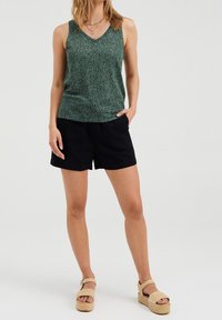 Vihreä kuvioitu toppi V-pääntiemällä, yhdistetty mustiin shortseihin. Beiget platform-sandaalit täydentävät asua.