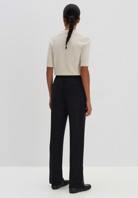 Beige shirt met korte mouwen gecombineerd met losse zwarte broek. De broek heeft een elastische tailleband en een gladde textuur.