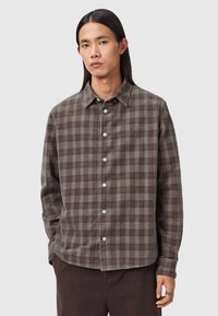 Braunes Karomuster-Hemd mit Button-Down-Kragen, aus weichem Stoff gefertigt, mit weißen Knöpfen und langen Ärmeln. Dezente Struktur im gesamten Stoff.