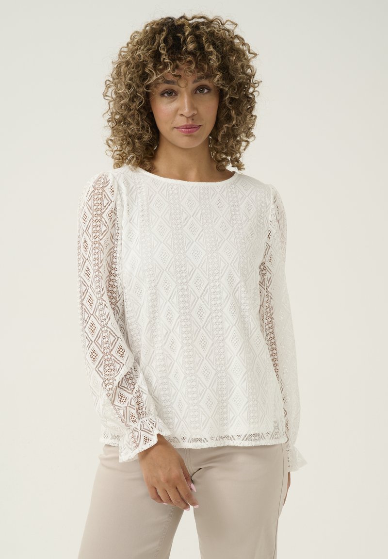 White long-sleeve blouse featuring a textured pattern with diamond shapes, sheer lace accents on sleeves, and a crew neckline.