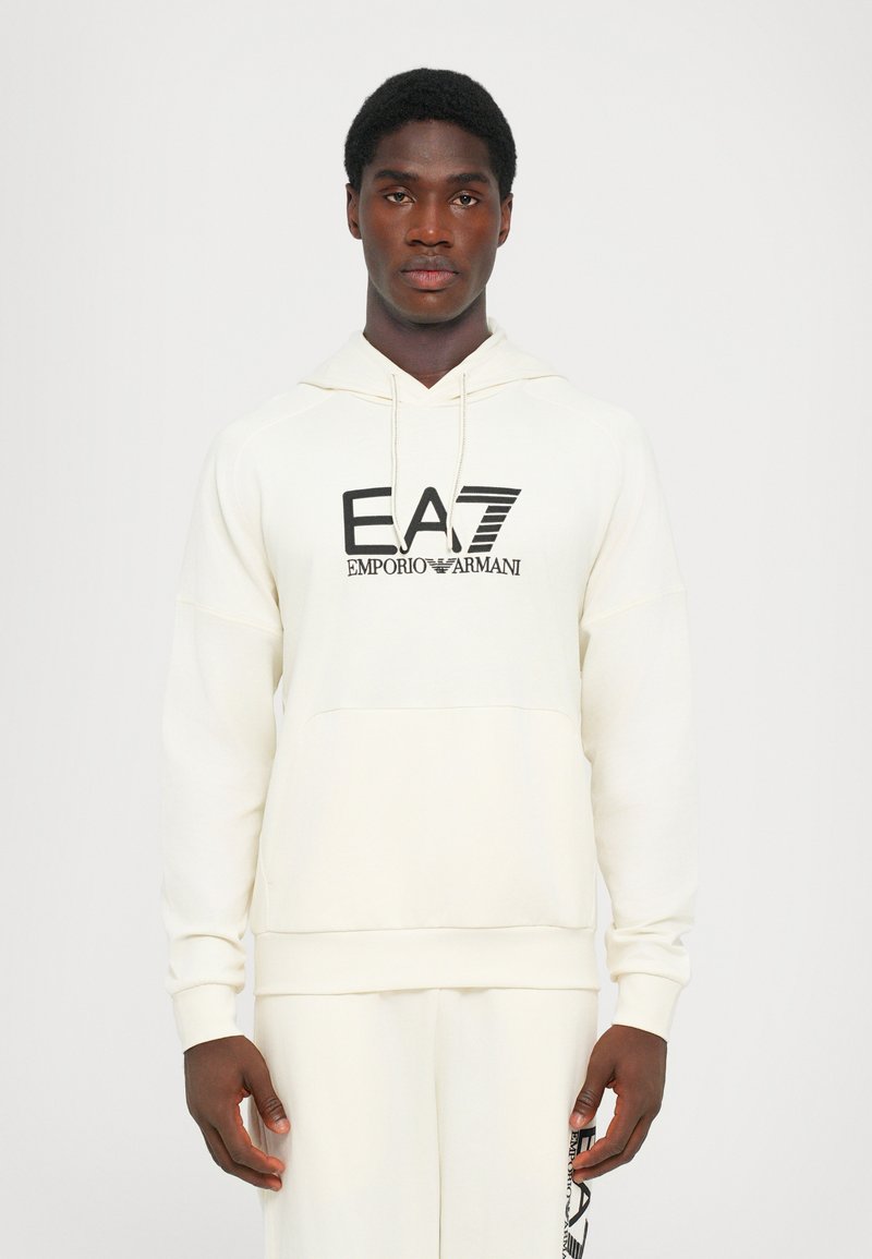 Felpa crema realizzata in tessuto morbido, con tasca a marsupio davanti, polsini a costine e logo nero "EA7 Emporio Armani".