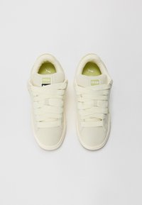 White canvas sneakers with textured upper, thick laces, and padded collar. Green insoles with Puma logo. Classic design and rubber sole.