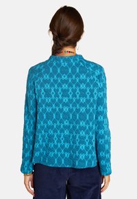 Türkisfarbene Jacke mit langen Ärmeln, geometrischem Muster, strukturiertem Stoff und runder Kragen; geschichtetem Designdetail am Saum.