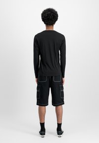 Svart langermet skjorte kombinert med svarte cargo-shorts med hvite sømmer, sidelommer og avslappet passform.