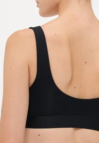 Close-up of a woman's upper back wearing a black tank top with wide straps, showing natural skin texture and moles.