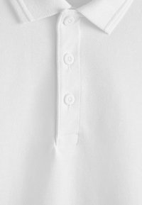 Gros plan sur un polo blanc montrant le tissu texturé, le col et trois boutons blancs sur la patte de boutonnage.