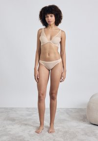 Γυμνό εσώρουχο σετ που περιλαμβάνει ένα ελαφρώς επενδυμένο σουτιέν με λεπτές τιράντες και αντίστοιχους μπικίνι, κατασκευασμένο από μαλακό, διάφανο ύφασμα.