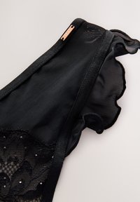 Sort gennemsigtigt lingeri med blonder og pailletdetaljer, flæsekant og en lille metalplade med teksten "Lipsy" på linningen.