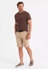 Chemise marron à manches courtes associée à un short beige, retroussé au niveau de l'ourlet, complétée par des chaussures décontractées grises. Design simple et épuré sans motifs.