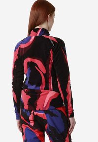 Maglione in pile con zip nero, caratterizzato da vivaci motivi astratti in rosso e blu, con colletto alto e dettaglio del logo sulla spalla.