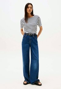 Top de mangas curtas às riscas, jeans largos azuis, cinto preto. O conjunto apresenta um design casual, com um corte descontraído e textura de denim.