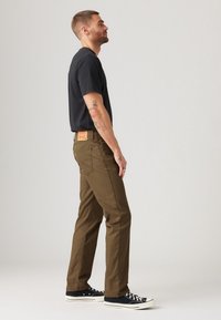 Khaki straight-leg pants made from cotton, featuring a leather logo patch on the back. Paired with a black t-shirt and black sneakers.