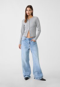 Grå långärmad cardigan med knappar, kombinerad med vida ljusblå denimjeans. Texturen är mjuk och passformen är avslappnad.