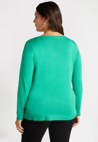 Zielony sweter z długim rękawem, o ściągaczu na dole i przy mankietach. Gładka tekstura, okrągły dekolt i nieco luźny krój. Brak widocznych wzorów lub akcentów.