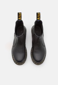 Black leather slip-on shoes with a textured surface, yellow stitching along the sole, and a black and yellow pull tab at the heel.