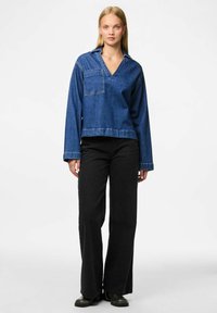 Denim puloveris ar V veida kaklu un garām piedurknēm, ar priekšējo kabatu, apvienots ar augsto jostasvietu melnām platu kāju biksēm un melnām zābakiem.