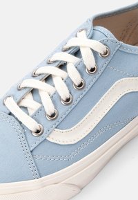 Baskets en toile bleu clair avec des lacets et des coutures blanches. Présentent des œillets en métal et un design de vague blanche sur le côté. Semelle en caoutchouc.