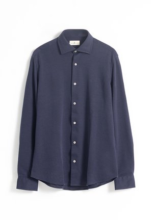 Camisa de manga larga en azul marino hecha de tela ligera. Cuenta con cuello abotonado, botones frontales y un dobladillo ligeramente curvado. Detalle sutil del logo.