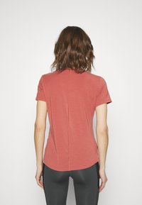 Camiseta de manga corta en tejido rosa apagado con dobladillo curvado, que presenta un detalle de costura central en la parte posterior, combinada con leggings negros.