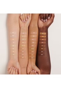 Trois bras présentant des teintes de peau variées avec des échantillons d'ombres de fond de teint étiquetés. Les couleurs vont du clair au foncé, incluant des sous-tons froids et chauds.