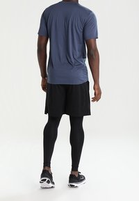 Mans sportiga kläder med en marinblå t-shirt med kort ärm och svarta shorts, samt åtsittande svarta leggings och löparskor.