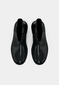 Schwarze glänzende Knöchelstiefel mit strukturierten Gummisohlen, die ein schlupffreies Design und seitliche Elastikpaneele für einfaches Tragen bieten.