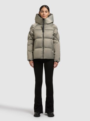 Vaaleanharmaa toppatakki, jossa on korkea, jäsennelty kaulus; laatikkomainen muoto; vetoketjusuljin; ja näkyvät sauma- ja ompelutiedot, puettuna mustujen, vartalonmyötäisten housujen päälle.